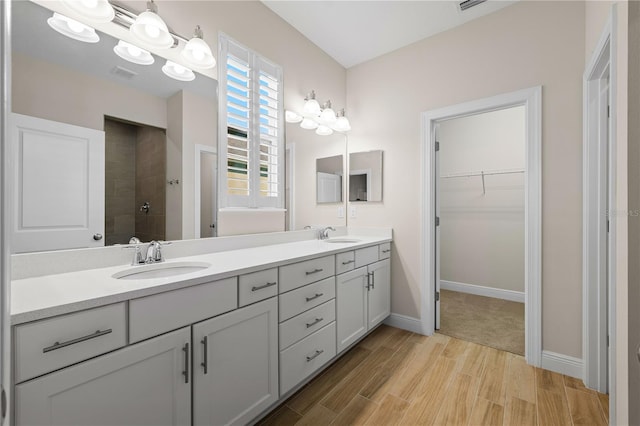 bathroom with double vanity, visible vents, wood finished floors, a tile shower, and a sink