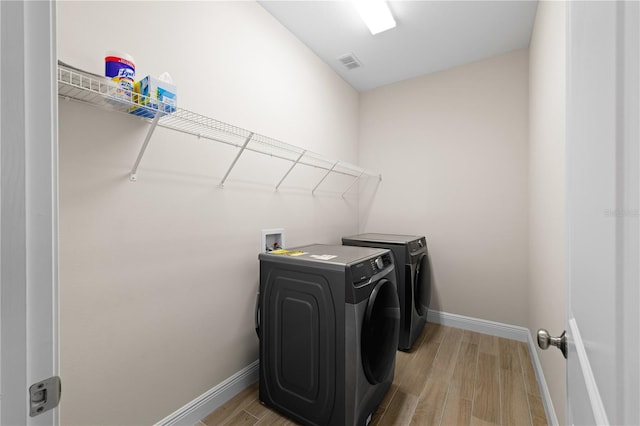 washroom featuring washing machine and dryer, laundry area, visible vents, baseboards, and light wood finished floors