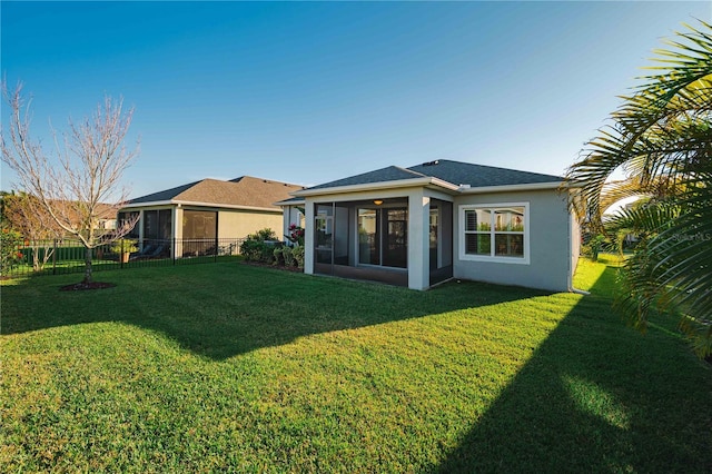 rear view of house with a sunroom, a lawn, fence, and stucco siding