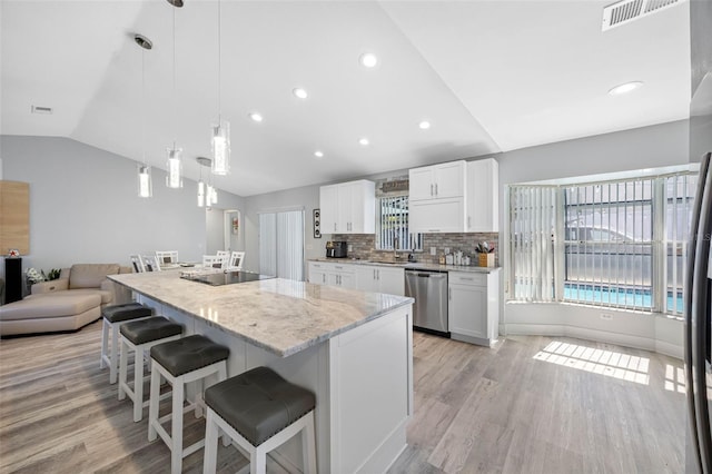 kitchen featuring light wood-style flooring, a breakfast bar, visible vents, vaulted ceiling, and dishwasher