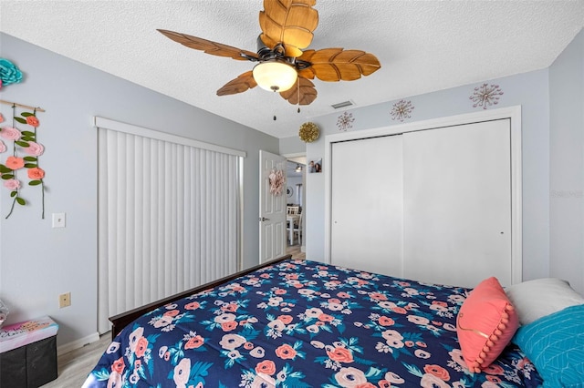 bedroom with a textured ceiling, ceiling fan, a closet, and visible vents