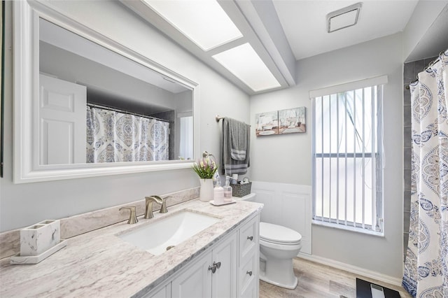 full bath with toilet, a wainscoted wall, wood finished floors, visible vents, and vanity