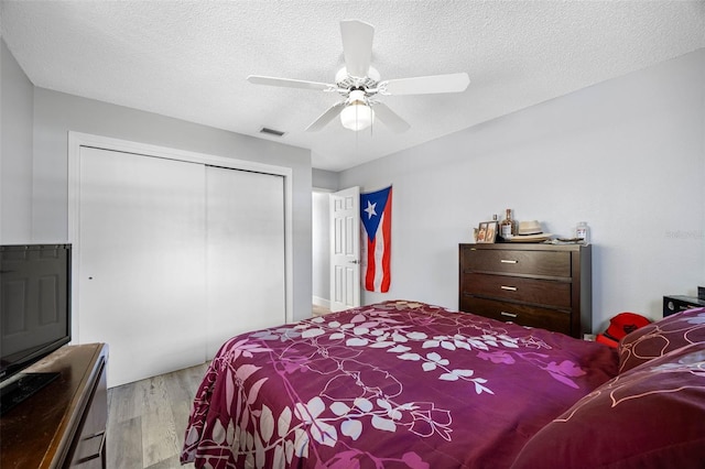 bedroom with a textured ceiling, wood finished floors, visible vents, a ceiling fan, and a closet