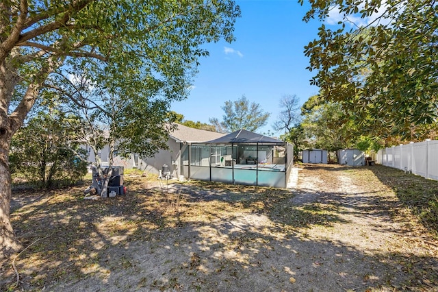 rear view of house with a storage shed, an outbuilding, fence, and a lanai