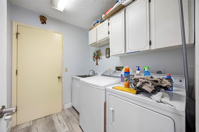 laundry area featuring cabinet space, light wood finished floors, independent washer and dryer, a textured ceiling, and a sink