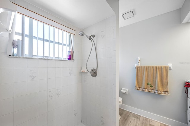 full bath featuring visible vents, toilet, a tile shower, wood finished floors, and baseboards