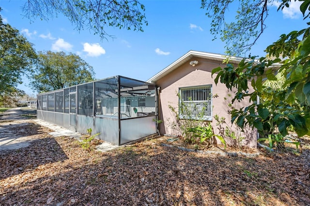 view of home's exterior with glass enclosure, a pool, and stucco siding