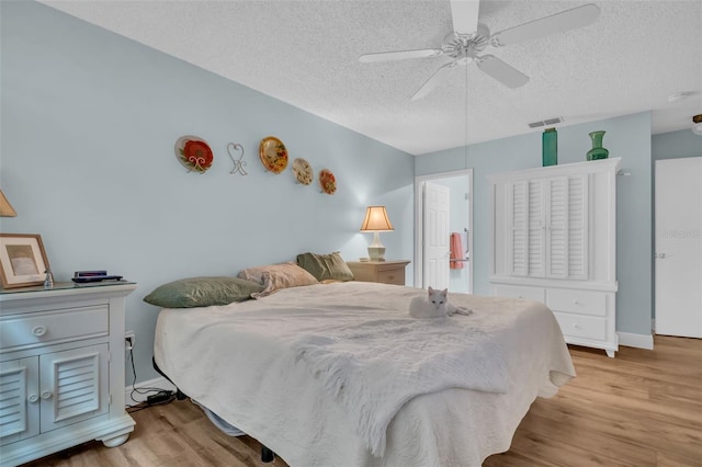 bedroom featuring light wood-type flooring, a ceiling fan, visible vents, and a textured ceiling