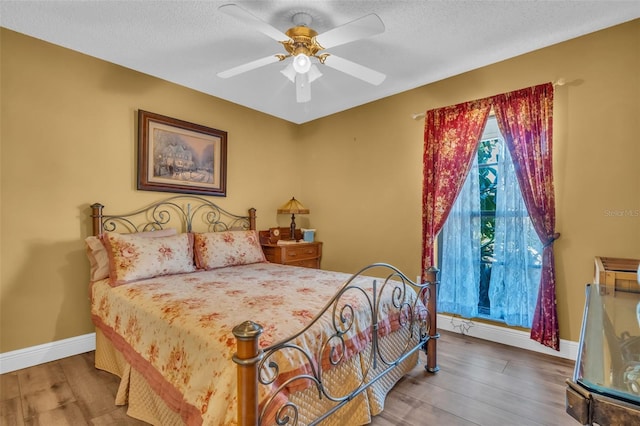 bedroom with a ceiling fan, a textured ceiling, baseboards, and wood finished floors