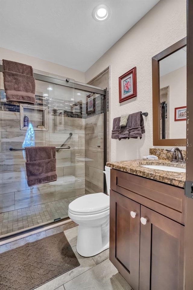 bathroom featuring toilet, a textured wall, a shower stall, and vanity