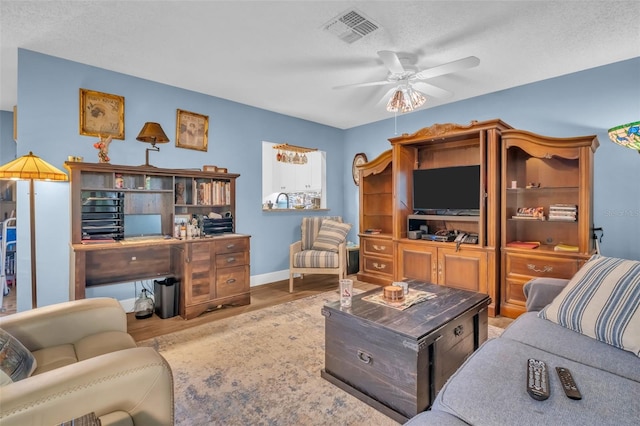 living area featuring a textured ceiling, wood finished floors, visible vents, baseboards, and a ceiling fan