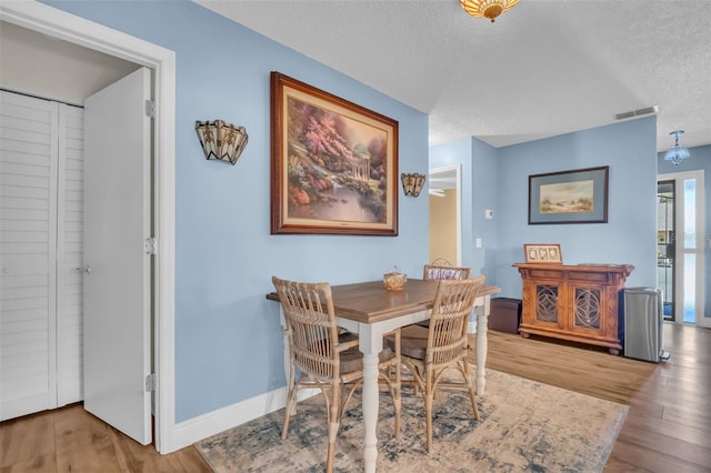 dining room featuring visible vents, a textured ceiling, baseboards, and wood finished floors