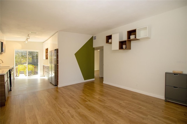 empty room featuring a sink, wood finished floors, visible vents, baseboards, and track lighting