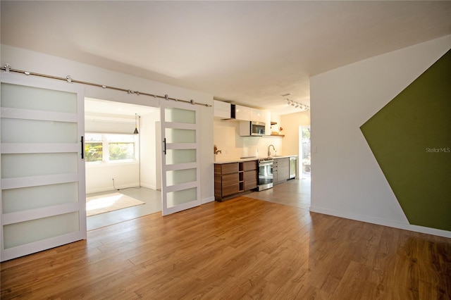 unfurnished living room with rail lighting, a barn door, baseboards, and wood finished floors