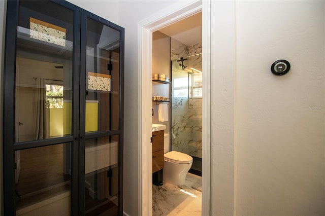 bathroom featuring toilet, marble finish floor, a marble finish shower, and vanity