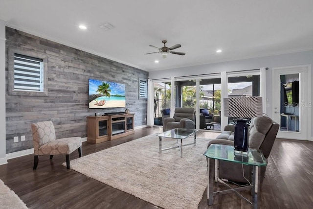 living room with an accent wall, recessed lighting, dark wood-type flooring, and crown molding