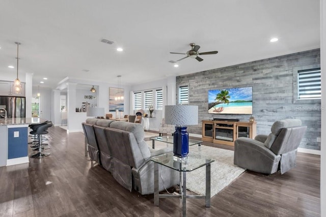 living area featuring an accent wall, dark wood-style flooring, decorative columns, and visible vents