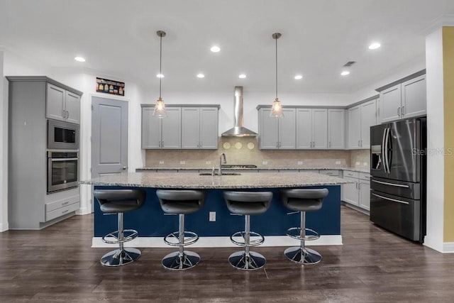 kitchen featuring appliances with stainless steel finishes, a sink, light stone counters, and wall chimney exhaust hood