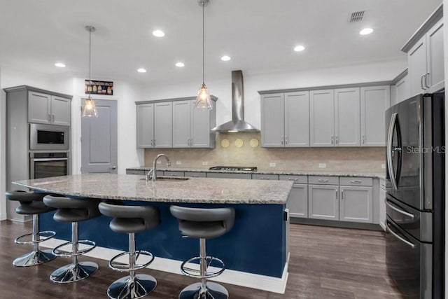 kitchen with visible vents, appliances with stainless steel finishes, a sink, light stone countertops, and wall chimney exhaust hood