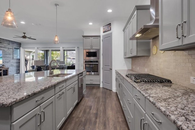 kitchen with gray cabinetry, a sink, appliances with stainless steel finishes, backsplash, and wall chimney exhaust hood