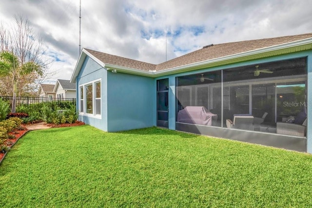 back of property with fence, a sunroom, roof with shingles, a lawn, and stucco siding