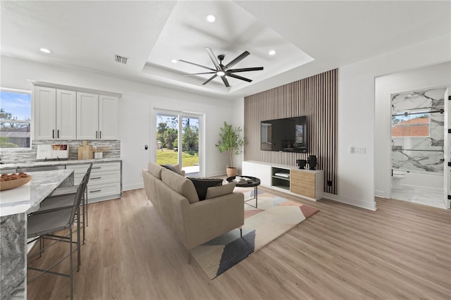 living area featuring light wood-style floors, a tray ceiling, and visible vents