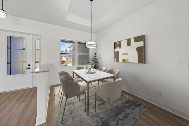 dining room featuring a tray ceiling, baseboards, and wood finished floors