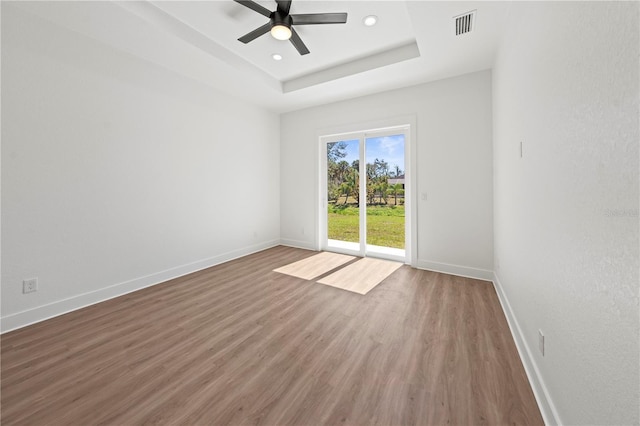 spare room featuring wood finished floors, a raised ceiling, visible vents, and baseboards