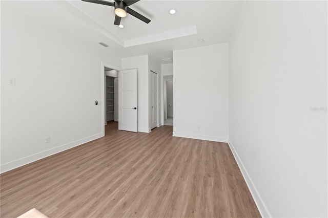 unfurnished bedroom with light wood finished floors, visible vents, baseboards, and a raised ceiling