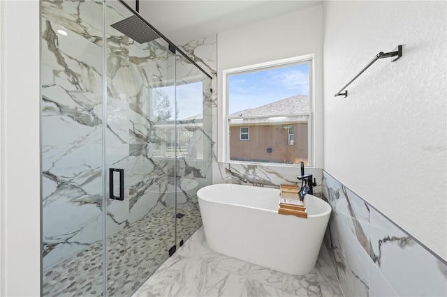 bathroom featuring a freestanding bath, marble finish floor, a marble finish shower, and tile walls