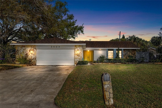 view of front of house featuring an attached garage, driveway, a front lawn, and stone siding