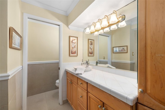 bathroom with toilet, a wainscoted wall, vanity, tile patterned floors, and crown molding