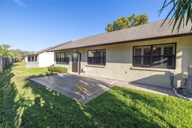 back of property featuring stucco siding, a lawn, a shingled roof, and fence