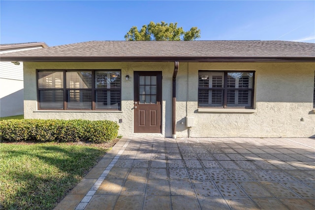 entrance to property with stucco siding and roof with shingles