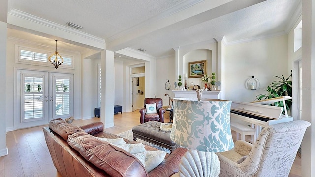 living room with a textured ceiling, light wood-style flooring, visible vents, french doors, and crown molding