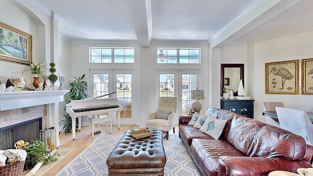 living room with a tiled fireplace, french doors, crown molding, a textured ceiling, and light wood-style floors