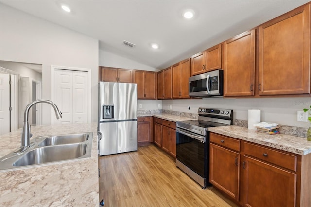 kitchen featuring light wood finished floors, lofted ceiling, light countertops, appliances with stainless steel finishes, and a sink