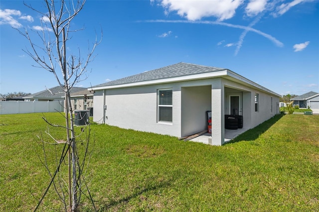 rear view of house featuring a patio, stucco siding, a lawn, central AC unit, and fence