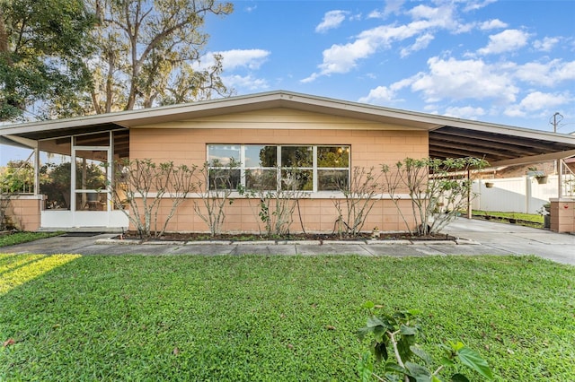 view of front of home featuring a carport, a front yard, a sunroom, and driveway