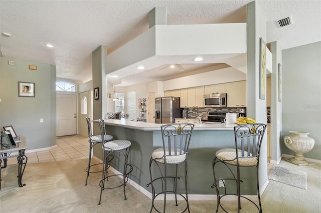 kitchen featuring a breakfast bar area, stainless steel appliances, visible vents, backsplash, and a peninsula