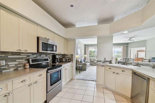 kitchen with light tile patterned floors, decorative backsplash, appliances with stainless steel finishes, open floor plan, and a sink