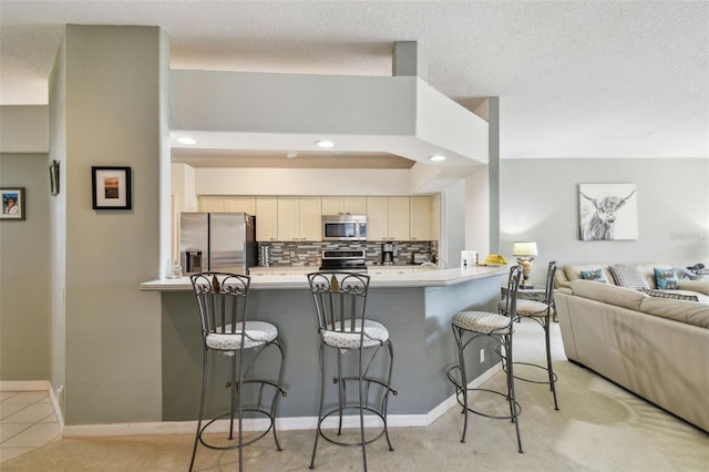 kitchen featuring a peninsula, tasteful backsplash, a kitchen bar, and appliances with stainless steel finishes