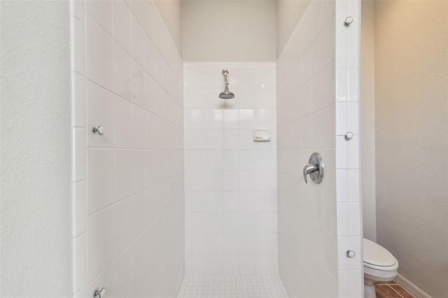 bathroom featuring a textured wall, toilet, and tiled shower