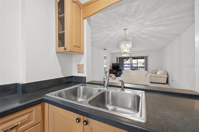 kitchen featuring dark countertops, glass insert cabinets, open floor plan, light brown cabinets, and a sink