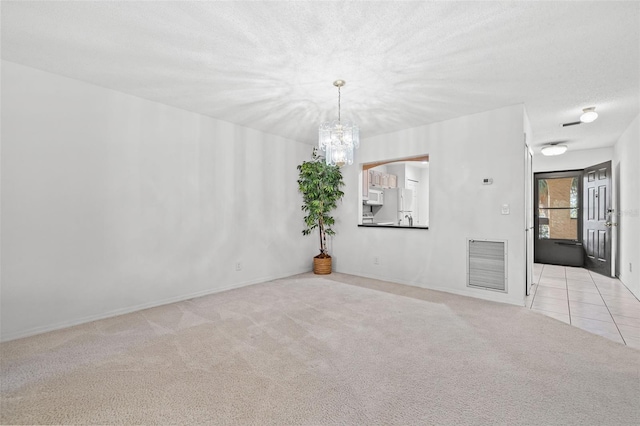 unfurnished room with visible vents, tile patterned flooring, carpet, a textured ceiling, and a chandelier