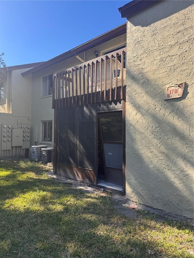 back of house with central air condition unit, a lawn, and stucco siding