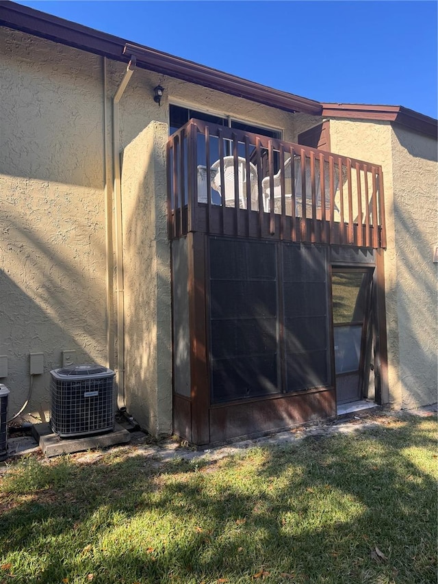 rear view of property with central AC, a yard, and stucco siding