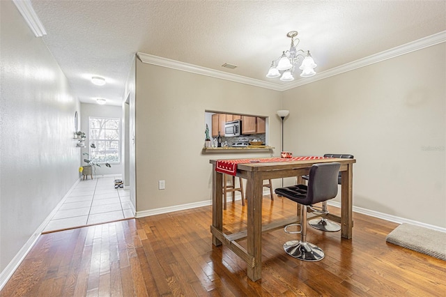 dining area with a chandelier, wood-type flooring, visible vents, and ornamental molding