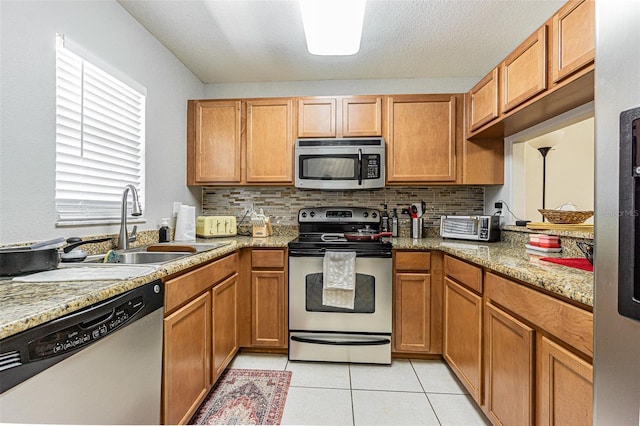 kitchen with light tile patterned floors, appliances with stainless steel finishes, a sink, and decorative backsplash