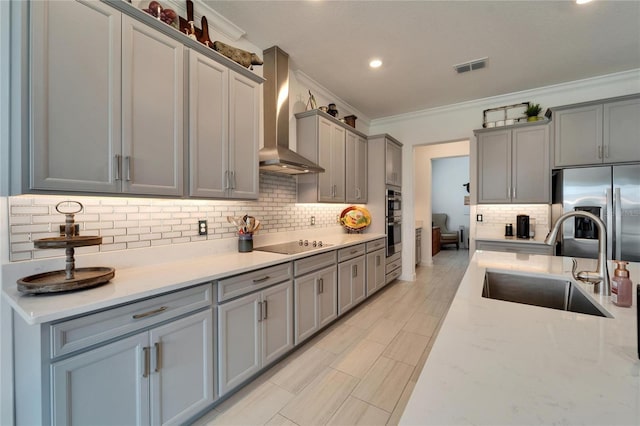 kitchen with a sink, appliances with stainless steel finishes, gray cabinets, wall chimney exhaust hood, and crown molding